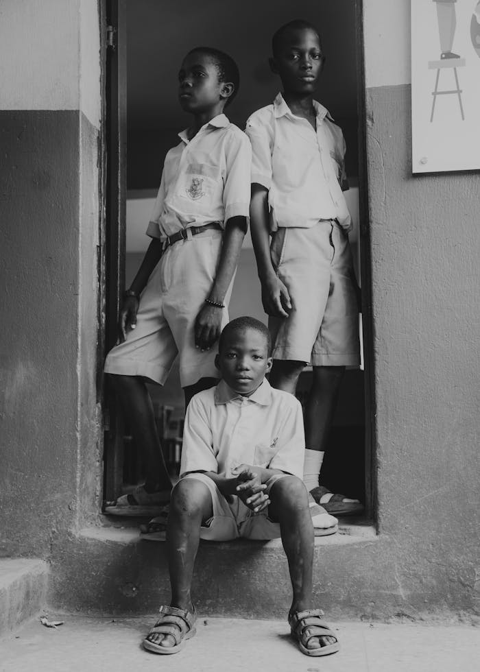 Black and white photo of three schoolchildren in uniform standing in a doorway.